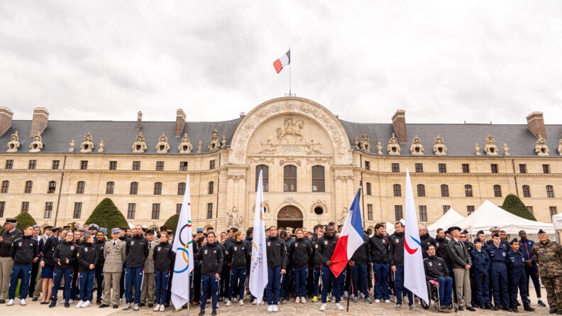 La tournée des drapeaux devant l'hôtel national des Invalides - nous voyons les drapeaux des JOP, le drapeau de Paris 2024 et le drapeau français. Il y a les SHND et des autorités des armées
