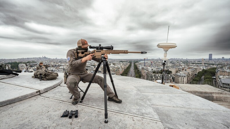 Au premier plan, un tireur d'élite du GIGN, cagoulé, assis, l'oeil dans la lunette de visée de son fusil. Au second plan, un second tireur d'élite dans la même position. Ils sont sur le toit d'un bâtiment surplombant Paris.