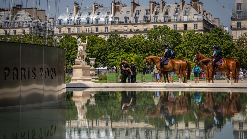 Devant un plan d'eau et un mur siglé Paris  2024 à gauche, 4 cavaliers et 3 gendarmes mobiles se font face