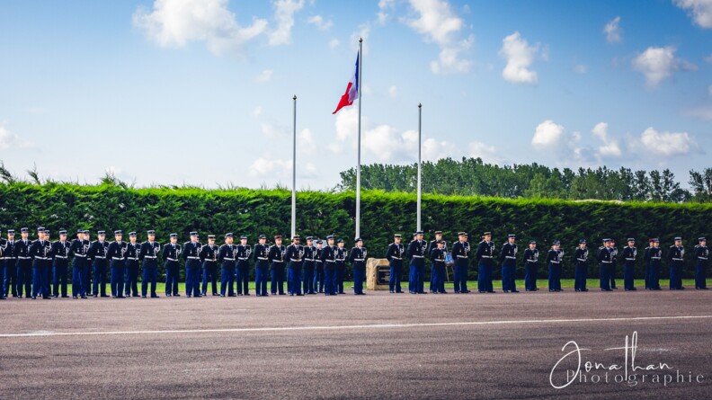 une promotion d'élèves-gendarmes en vareuse rassemblée, de part et d'autre du mât du drapeau français