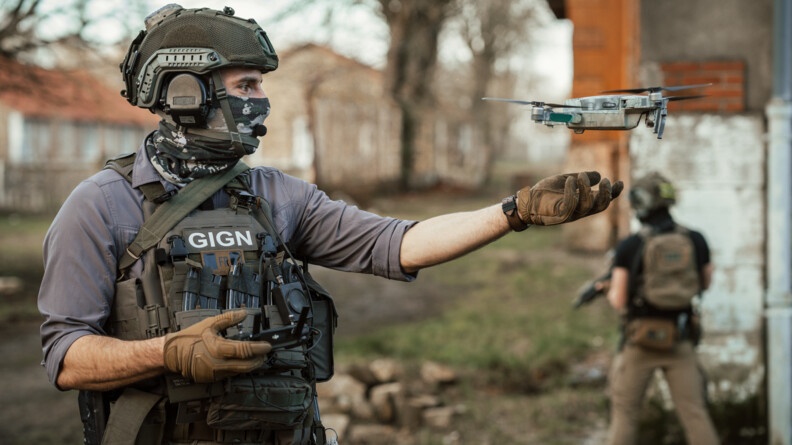 Militaire du GIGN avec un drone volant au-dessus de sa main gauche.