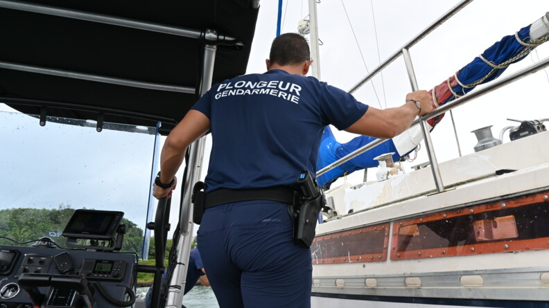 Un plongeur de la gendarmerie de dos s'apprête à monter sur un voilier lors d'une opération de contrôle.