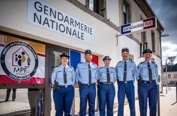 Cinq gendarmes debout les mains dans le dos devant la maison de protection des familles de Trégunc. Au dessu de l'entrée l'inscription "gendarmerie nationale" et sur la vitre le logo et la maison de protection des familles