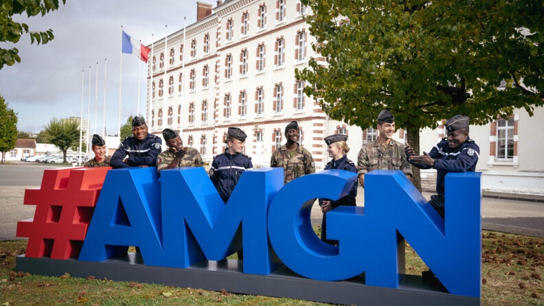 Huit élèves de l'Académie militaire de la gendarmerie nationale, quatre des pays amis de la France et quatre français, posent devant l'Académie, derrière le logo bleu et rouge.