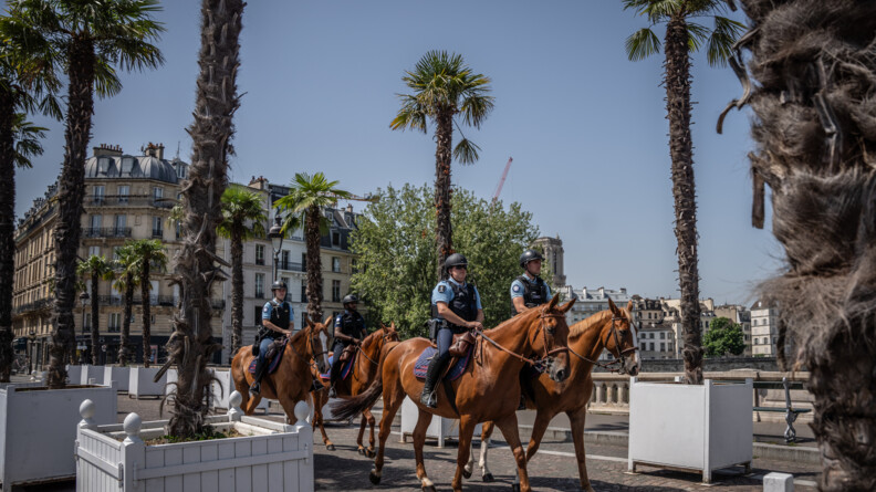 Sur un pont décoré de palmiers, 4 cavaliers de la gendarmerie marchent au pas sous le ciel bleu