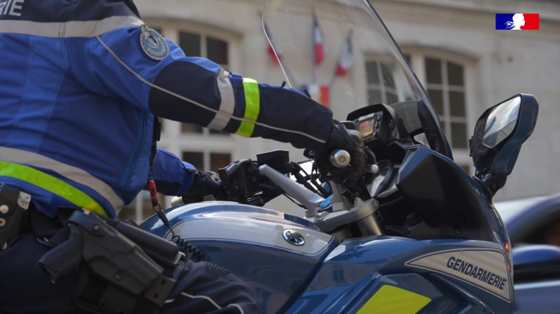 Une moto de la gendarmerie, avec un gendarme au volant, dont on ne voit pas la tête, sont photographiés en gros plan, de biais