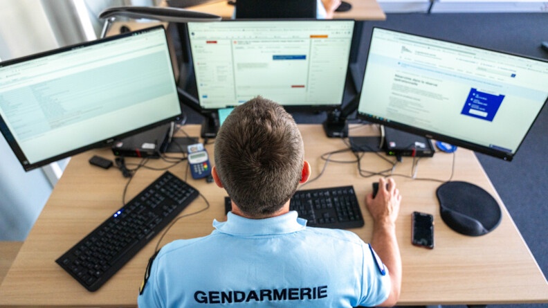 Vue en plongée d'un gendarme à son bureau face à trois écrans