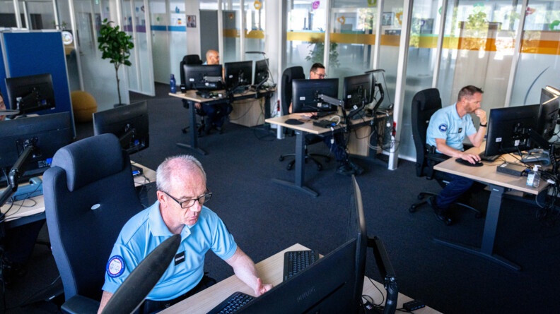 Vue d'ensemble de conq gendarmes derrières leurs écrans sur des bureaux; les murs le long des couloirs sont en verre