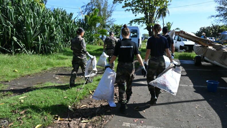 Cinq gendarmes de dos rammassent des déchets.