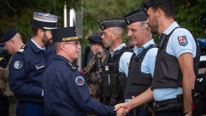 Le Major Général de la Gendarmerie Nationale serre la main à un gendarme. D'autres militaires de la gendarmerie et de l'armée de Terre, se tiennent debout à leurs côtés