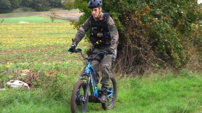 Un gendarme en treillis sur un vélo éclectrique sur un chemin herbeux