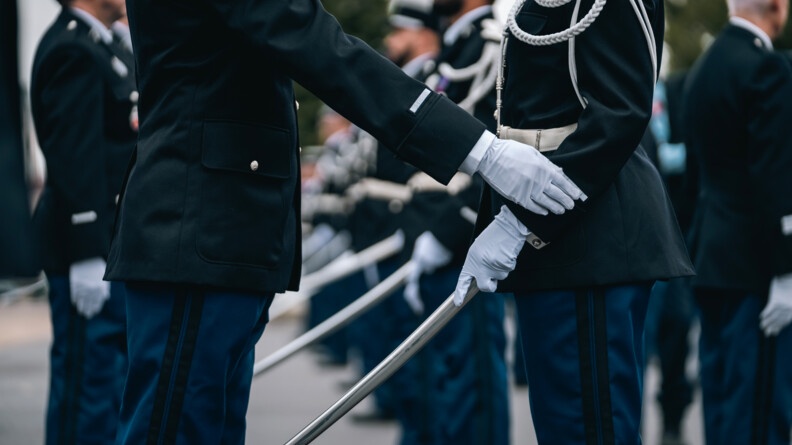 deux gendarmes face à face en tenue de cérémonie, l'un a le foureau relevé, l'autre touche son galon de manche