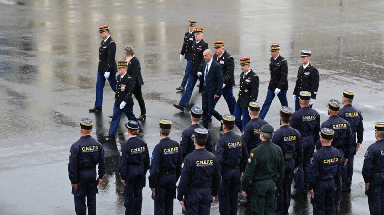 Une dizaine d'officiers généraux de gendarmerie défilent devant les personnels du CNEFG vu de dos, en combinaison floquée CNEFG