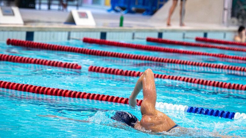 Une nageuse nage le crawl dans un bassin olympique. Sa tête est immergée dans l'eau. Elle porte un bonnet bleu marine.