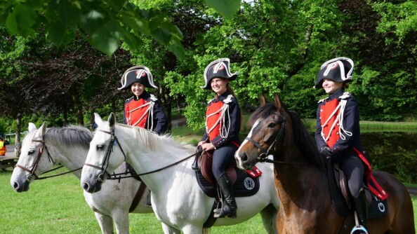 Trois militaires femmes se tiennent sur leur cheval à l'arrêt. Elles posent souriantes face à l'objectif.