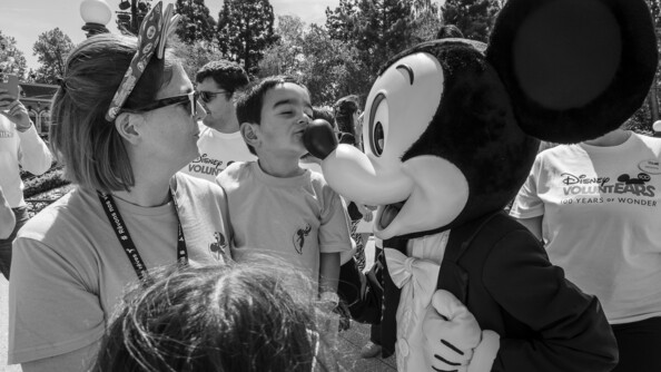 Une femme vêtu du -tshirt des Képis Pescalune, tient un enfant dans les bars, qui embrasse le nez de la mascotte Mickey à Disneyland Paris