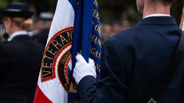 On aperçoit un militaire de dos, en uniforme bleu marine, tenant dans sa main droite gantée un drapeau tricole