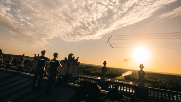 Deux gendarmes sur le toit regarde vers le ciel au soleil couhcant tandis que la patrouille de Francepasse laissant un sillon tricolore