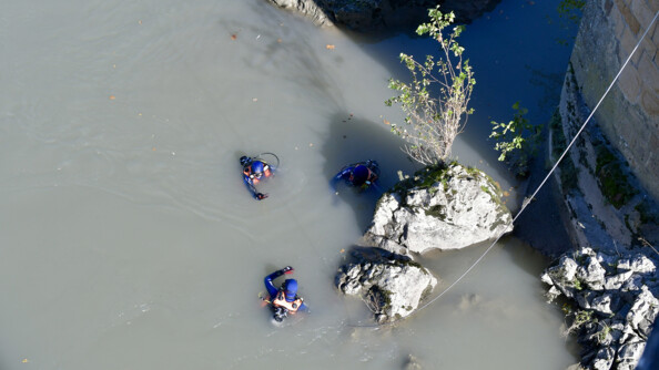 Trsois plongeurs de la gendarme à gauceh d'un rocher dans un cour d'eau au pied d'une colonne de pont