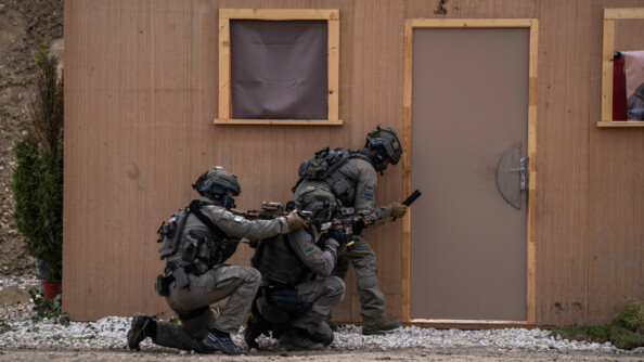 Trois militaires du GIGN en tenue kaki s'apprêtent à mettre des explosifs au pied d'une porte d'un préfabriqué en bois
