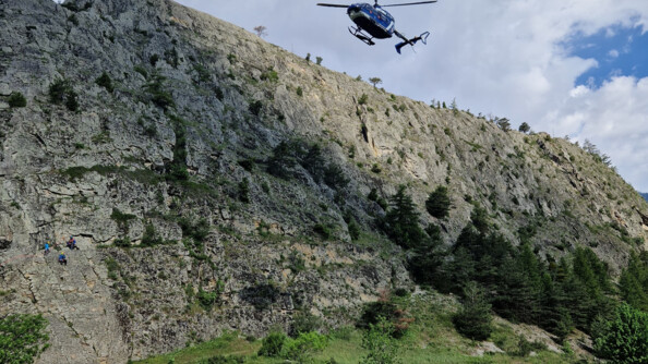 Un hélicoptère gendarmerie survole la vallée tandis que deux gendarmes arborant une chasuble orange marchent dans la vallée