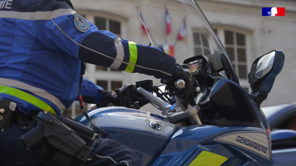 Une moto de la gendarmerie, avec un gendarme au volant, dont on ne voit pas la tête, sont photographiés en gros plan, de biais