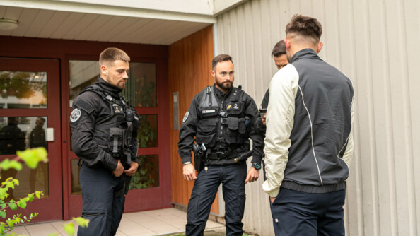 Des gendarmes discutent avec un habitant, que l'on aperçoit de dos. Tous se tiennent debout, devant la porte d'un immeuble.