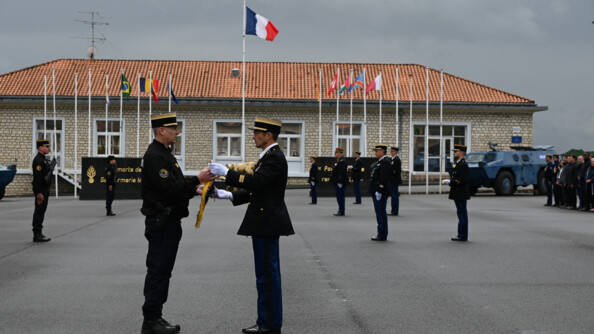 Devant d'autres gendarmes, un colonel de gendarmerie mobile re met à un commandant le fanion de son unité
