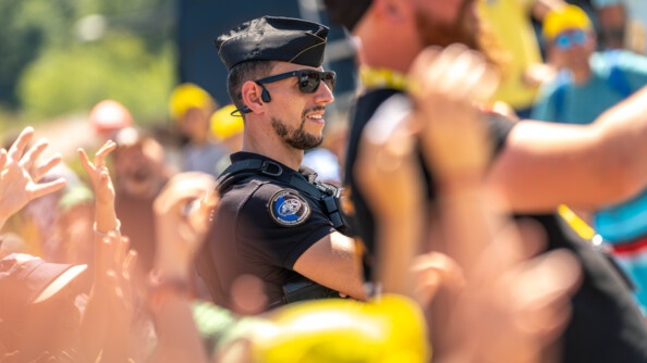 Un gendarme, revêtant un uniforme noir, se tient debout, au milieu d'une foule très dense. Le temps est ensoleillé.