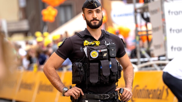 Un gendarme, revêtant un uniforme noir, se tient debout sur la route, mains sur les hanches, face à l'objectif. Derrière lui on aperçoit une grande bannière jaune, sur laquelle est inscrit "CONTINENTAL"