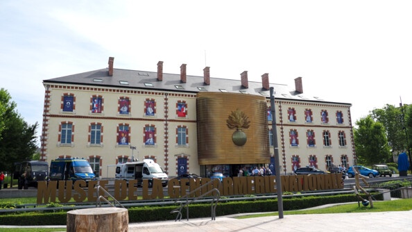 Le musée de la gendarmerie nationale avec à ses fenêtres les portraits des sportifs de haut-niveau de la gendarmerie et des véhcilue récents et anciens de la gendarmerie. Devant, deux rondins de bois ornés des chffres 1 et 3