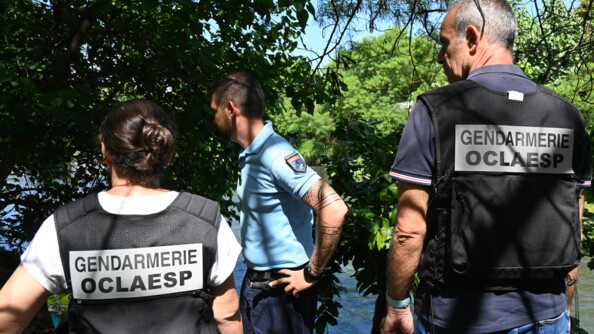 Trois gendarmes, dont deux de l'OCLAESP, de dos au bord d'une rivière.