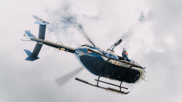 Vue en contre plongée d'un  hélicoptère gendarmerie dans le ciel nuageux, un gendarme à la porte latérale lançant un lest