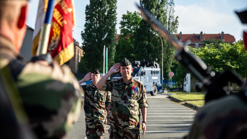 Agrandir l'image Le Général Christophe Daniel en treillis kaki au garde à vous. Au premier plan, dos, la garde au drapeau du GBGM.