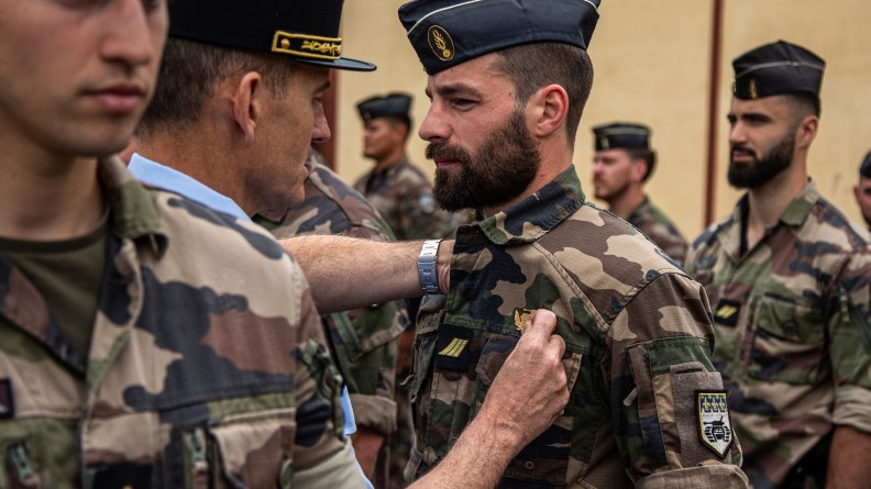 Agrandir l'image Un général, de dos, épingle un brevet sur la poitrine d'un militaire en treillis kaki.